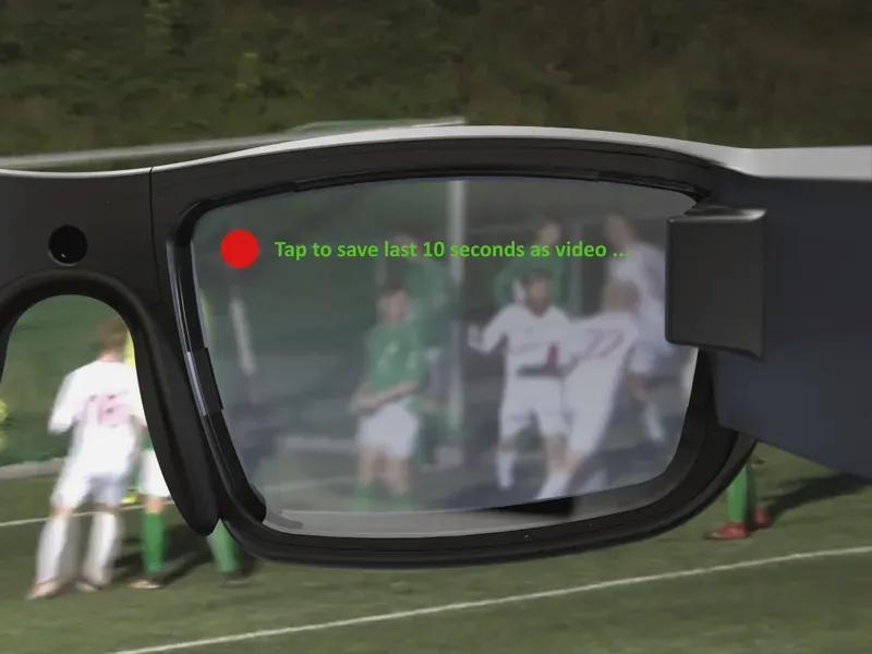Close-up of smart glasses at a football match; the lens shows a red record dot and the text "Tap to save last 10 seconds as video ..."
